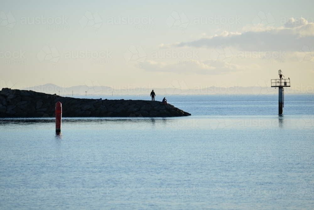 Fishermen fishing off the rocks at the end of a pier in the bay - Australian Stock Image