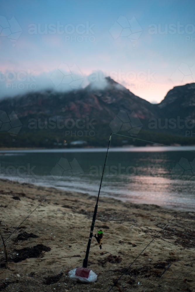 Fishing rod on beach at sunset with mountains and mist in background - Australian Stock Image