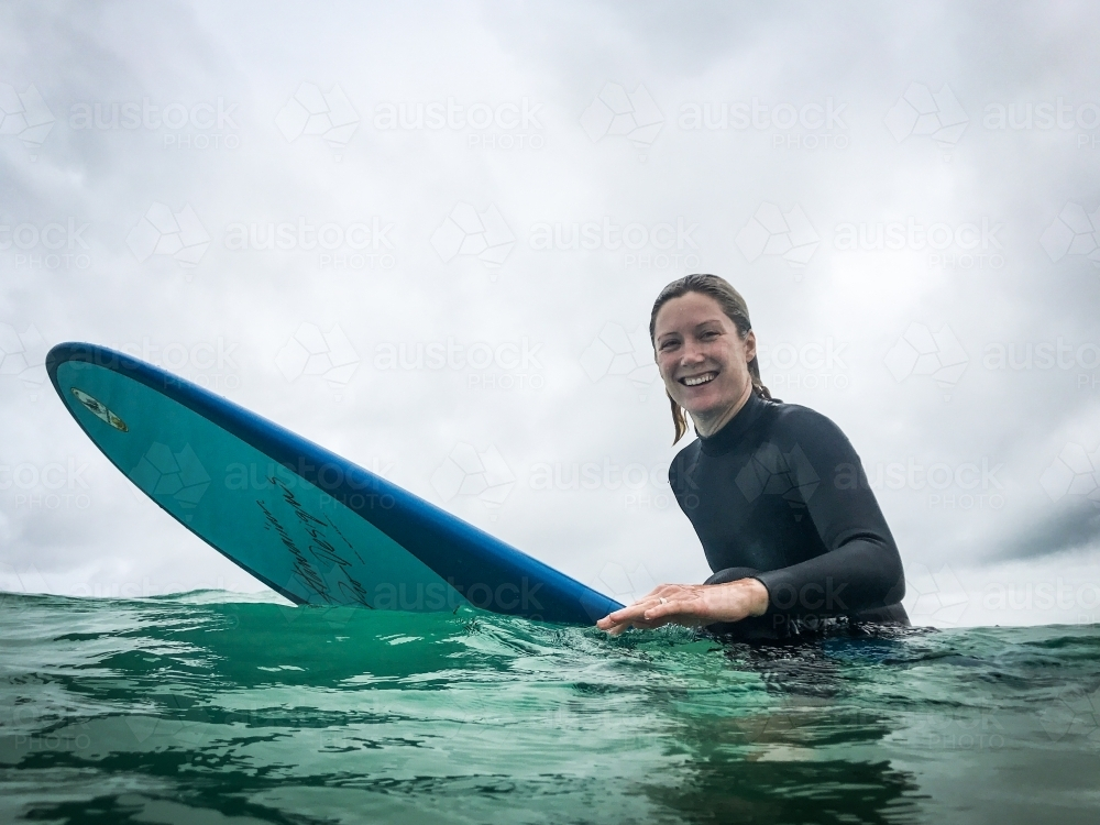 Fit, healthy natural woman sitting on longboard surfboard on overcast day - Australian Stock Image