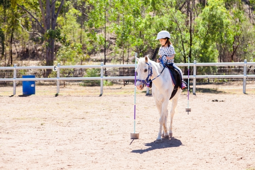 Five year old horse rider doing pole bending on white pony - Australian Stock Image