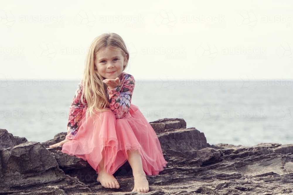 Five year old sitting on rocks blowing a kiss - Australian Stock Image