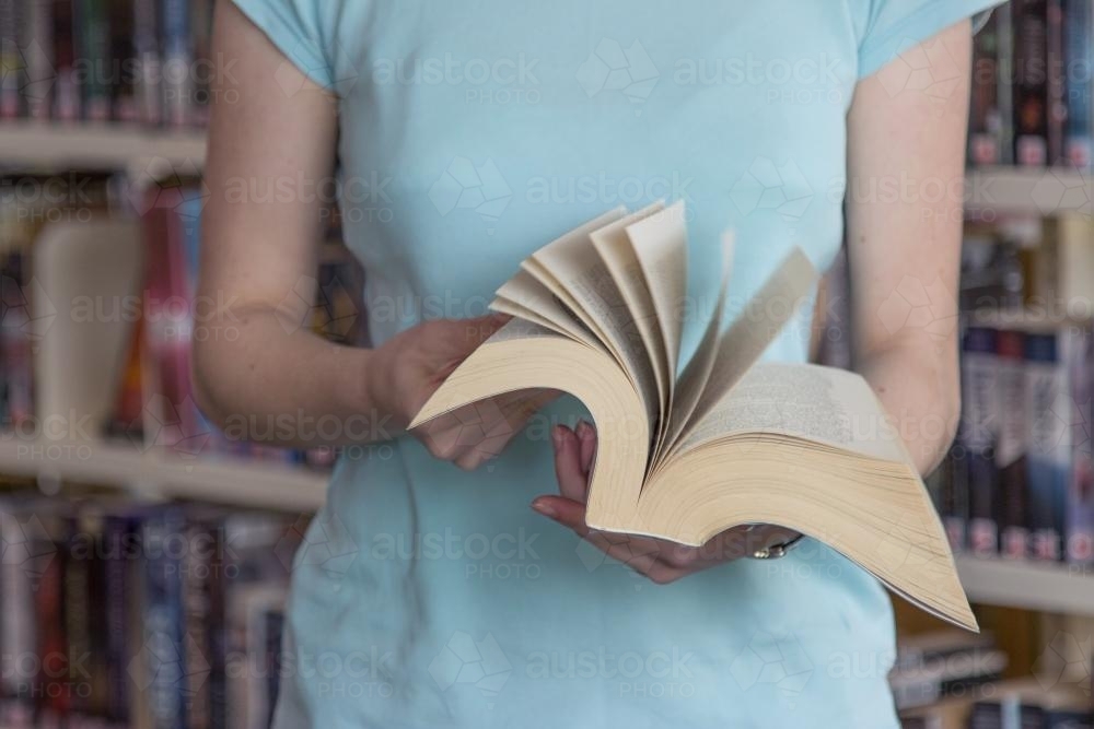 Flicking through the pages of a large book at the library - Australian Stock Image