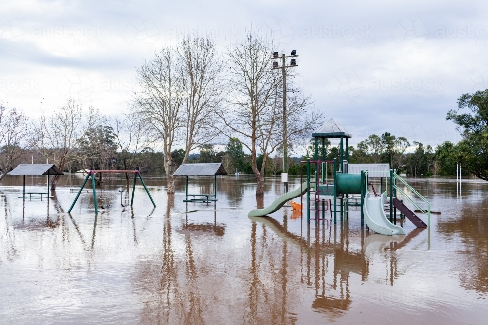 flood water covering picnic area and park play equipment during natural disaster of flood - Australian Stock Image