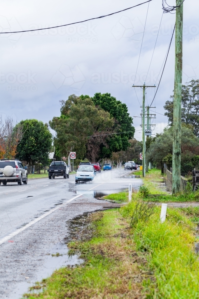 Flood water forming puddle on highway road through town with car driving through - Australian Stock Image