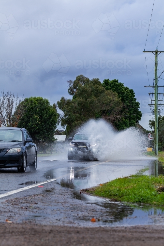 Flood water forming puddle on highway road through town with car driving through - Australian Stock Image