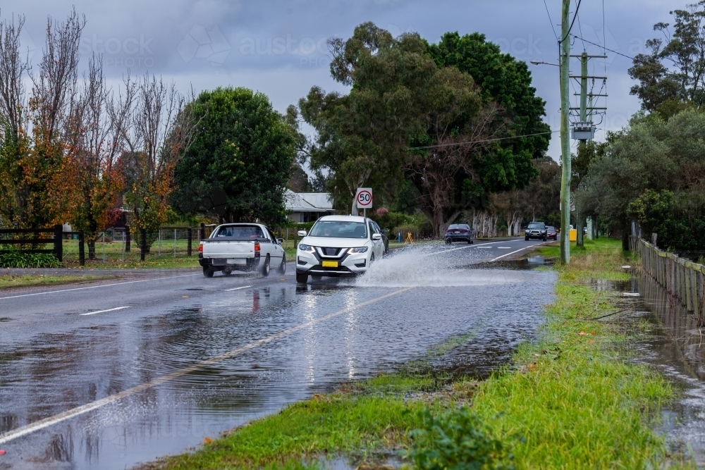 Flood water forming puddle on highway road through town with car driving through - Australian Stock Image