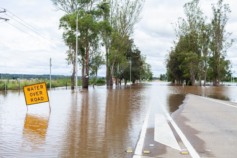 Floodwater rising over water over road sign on highway - Australian Stock Image