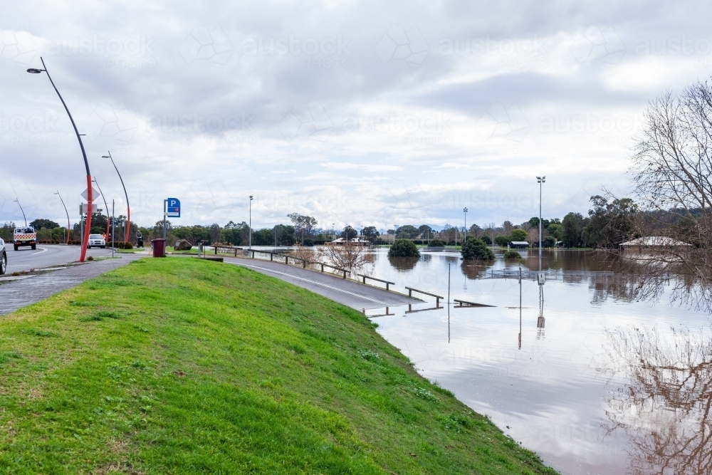 Floodwater rising up levee bank towards town during natural disaster event - Australian Stock Image