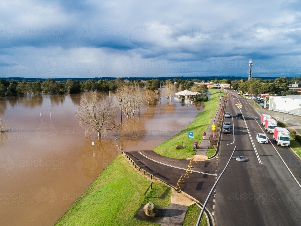 floodwaters covering riverside park beside township rising up levee bank - Australian Stock Image