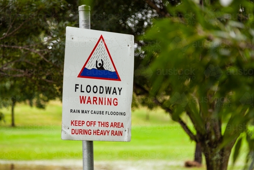 Floodway warning sign with rising water behind on rainy day - Australian Stock Image