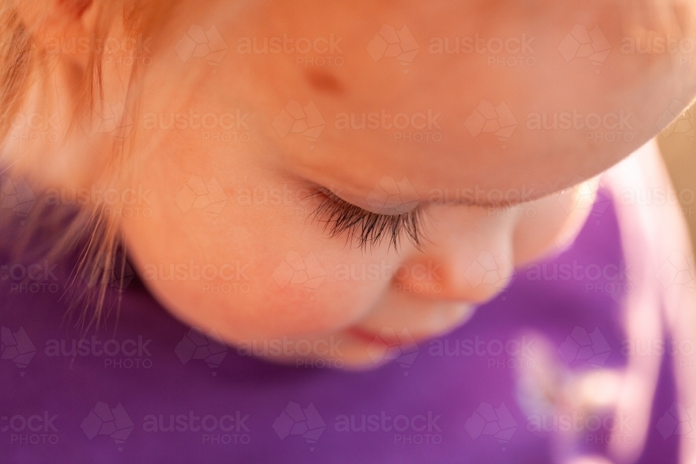 Focus on eyelash of toddler girl  looking down in sunshine outside - Australian Stock Image
