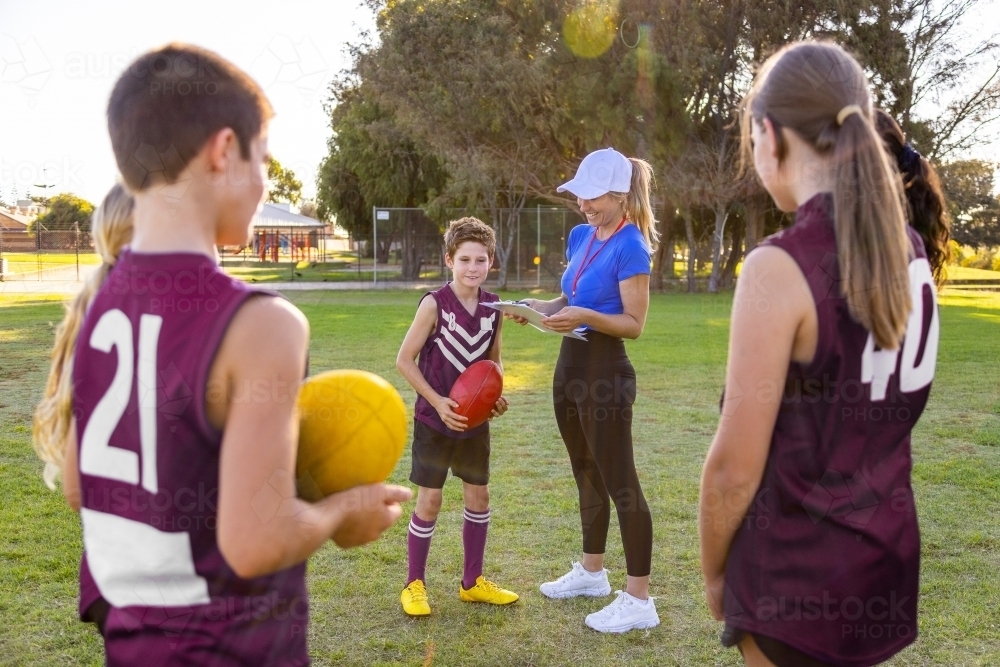 football coach talking to young kid with teammates looking on - Australian Stock Image