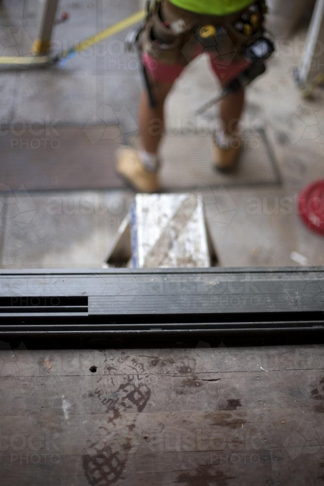 Footprints on wooden floorboards and tradesman working on deck at a home renovation site - Australian Stock Image