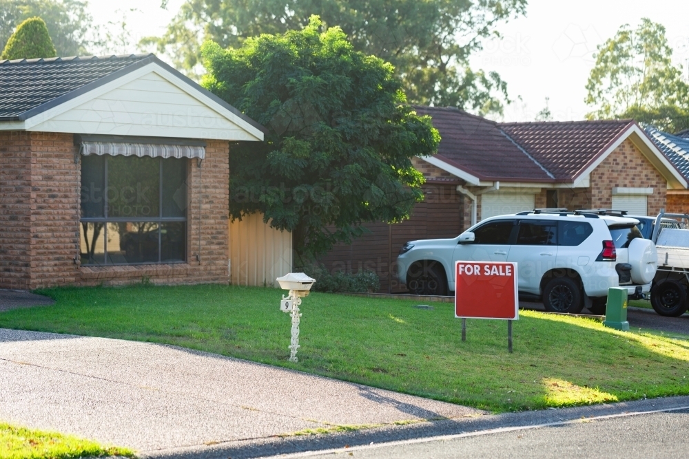 for sale sign on front lawn of home in residential area - Australian Stock Image