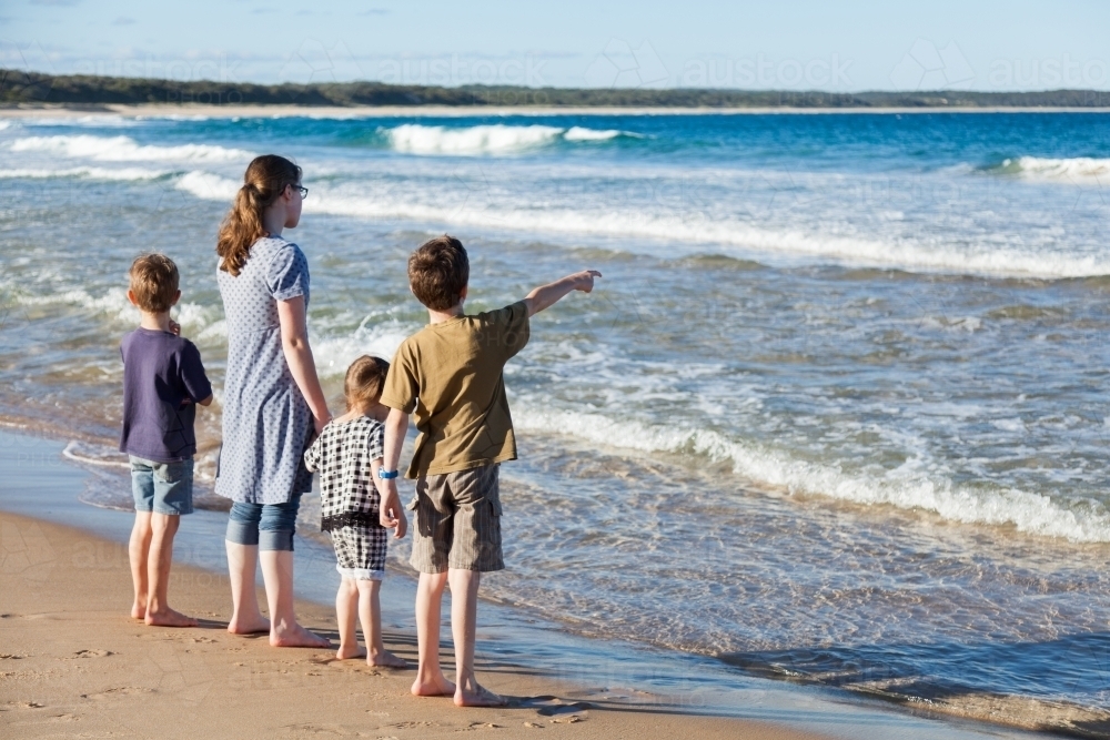 Four children holding hands and looking out to sea at beach - Australian Stock Image