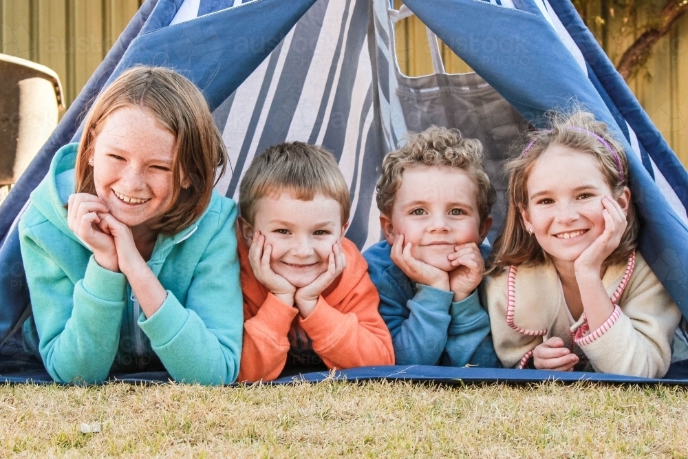 Four children lying in teepee tent smiling happy - Australian Stock Image