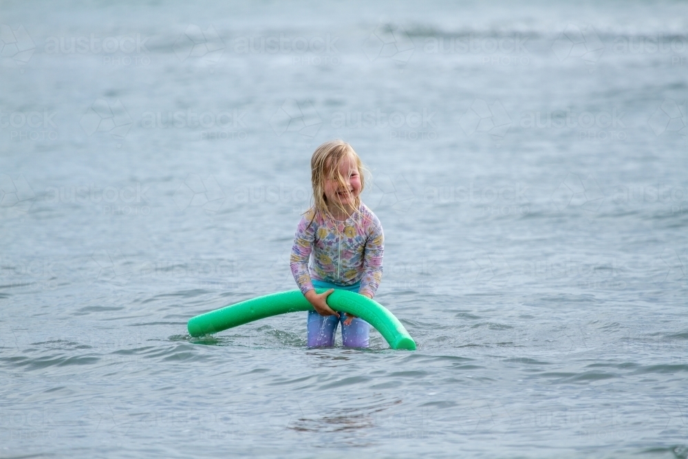 Four year old girl smiling and holding floatation noodle in the sea - Australian Stock Image