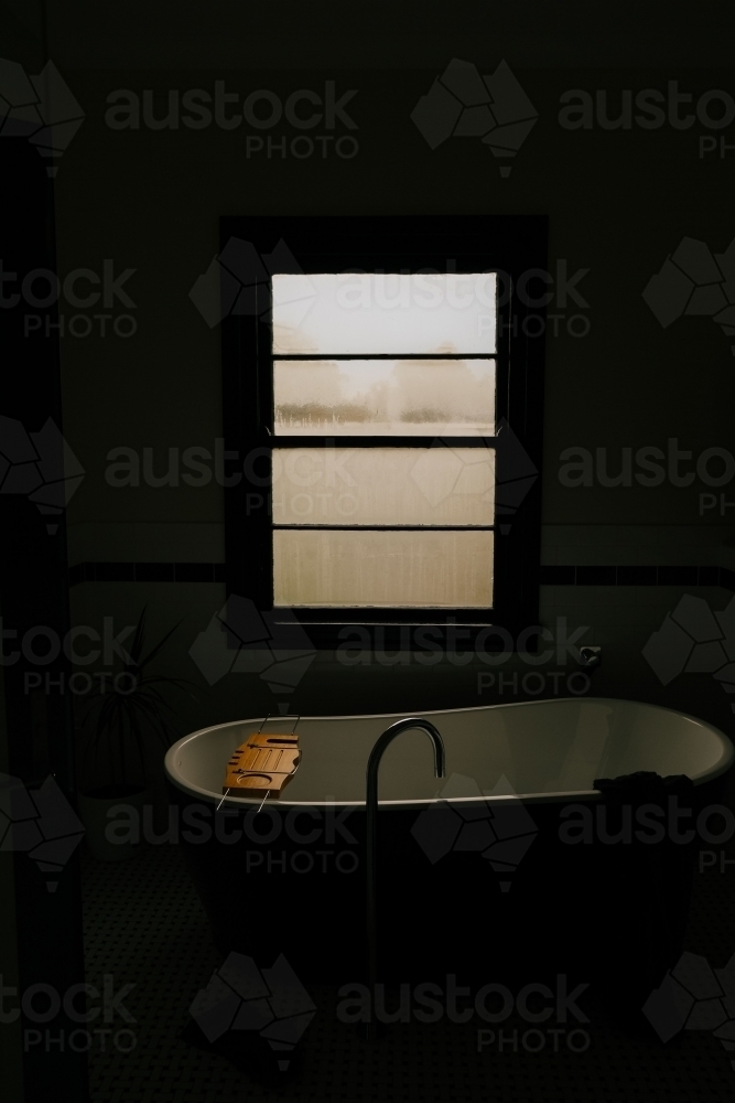 Freestanding bathtub with a wooden tray located near the window - Australian Stock Image