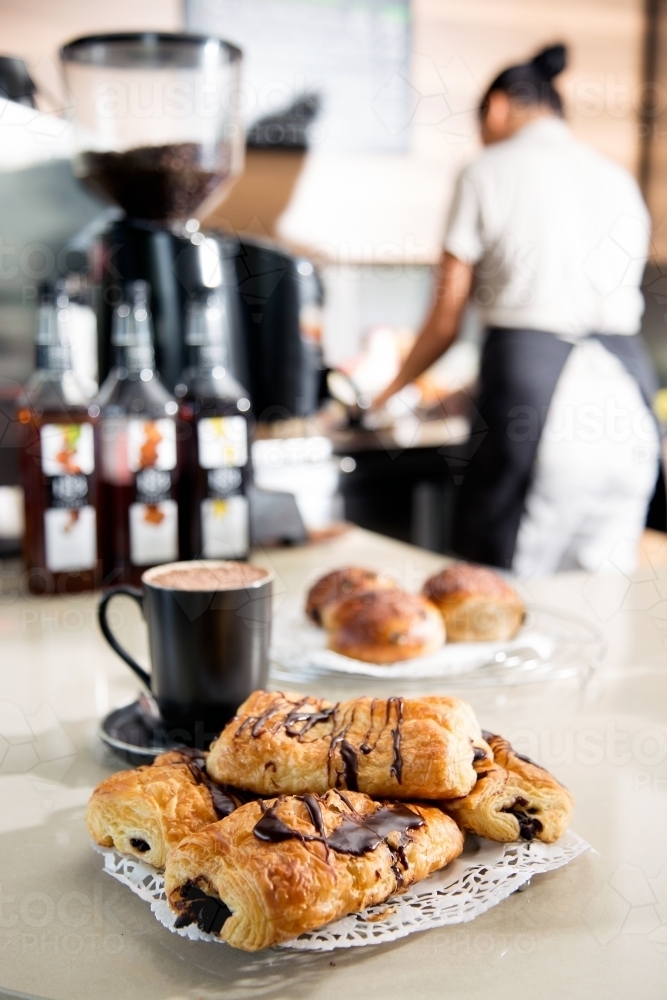 Fresh pastries on the counter of a cafe with workers in background - Australian Stock Image