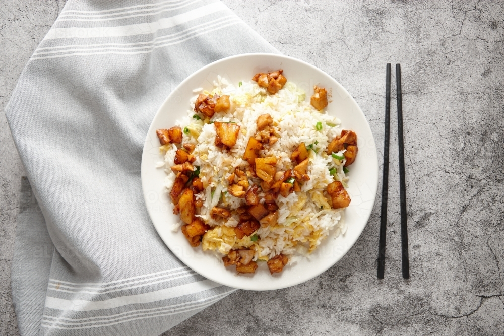 Fried rice topped with pineapple chicken served in a white plate. - Australian Stock Image