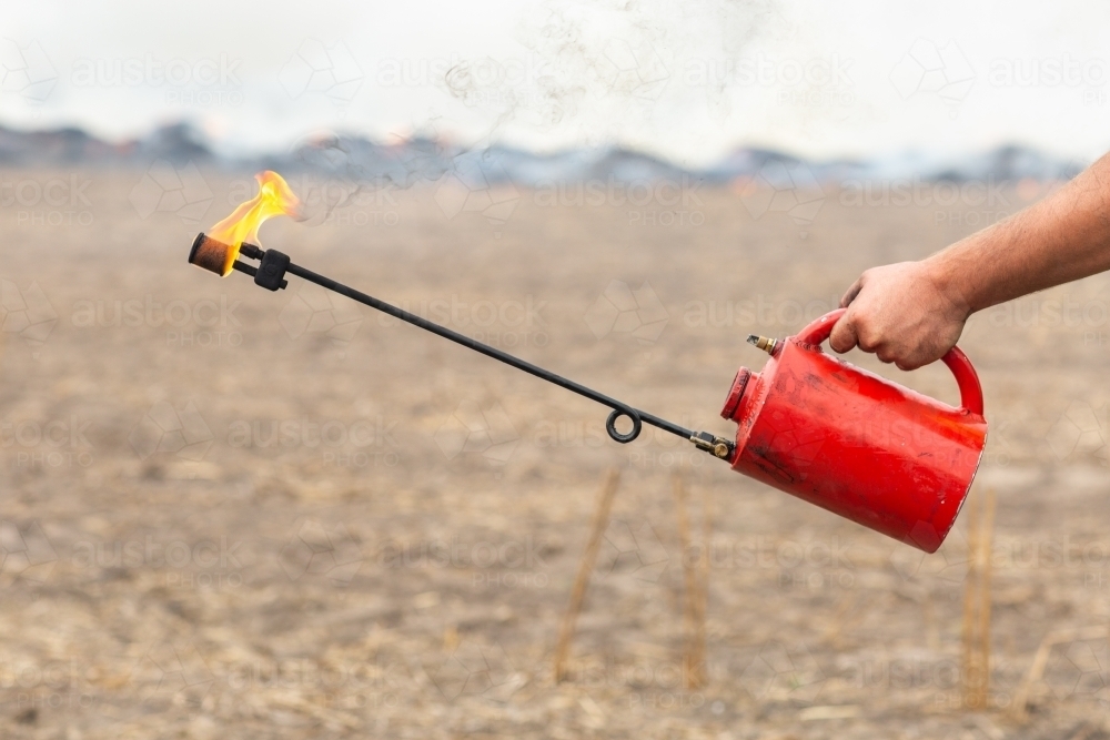 Fuel-filled fire-lighter with burning stubble in background - Australian Stock Image