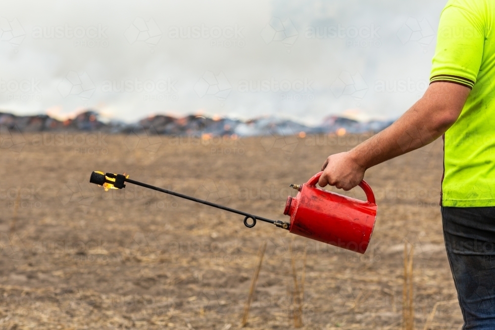 Fuel-filled fire-lighter with burning stubble in background - Australian Stock Image