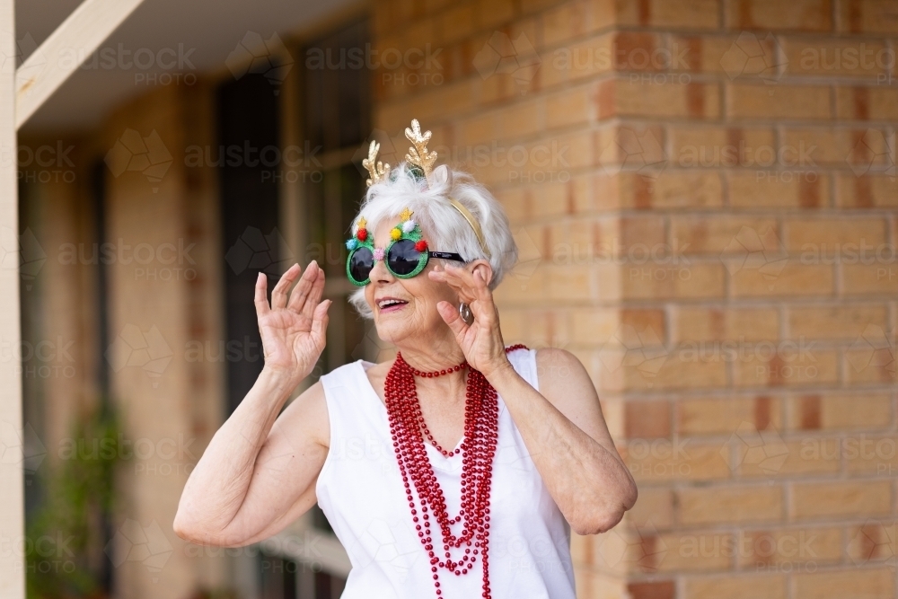 fun-loving elderly lady dressed up in reindeer antlers and fancy glasses at xmas - Australian Stock Image