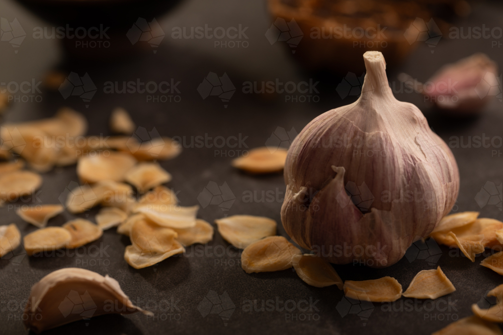 Garlic bulb and garlic chips on dark benchtop - Australian Stock Image
