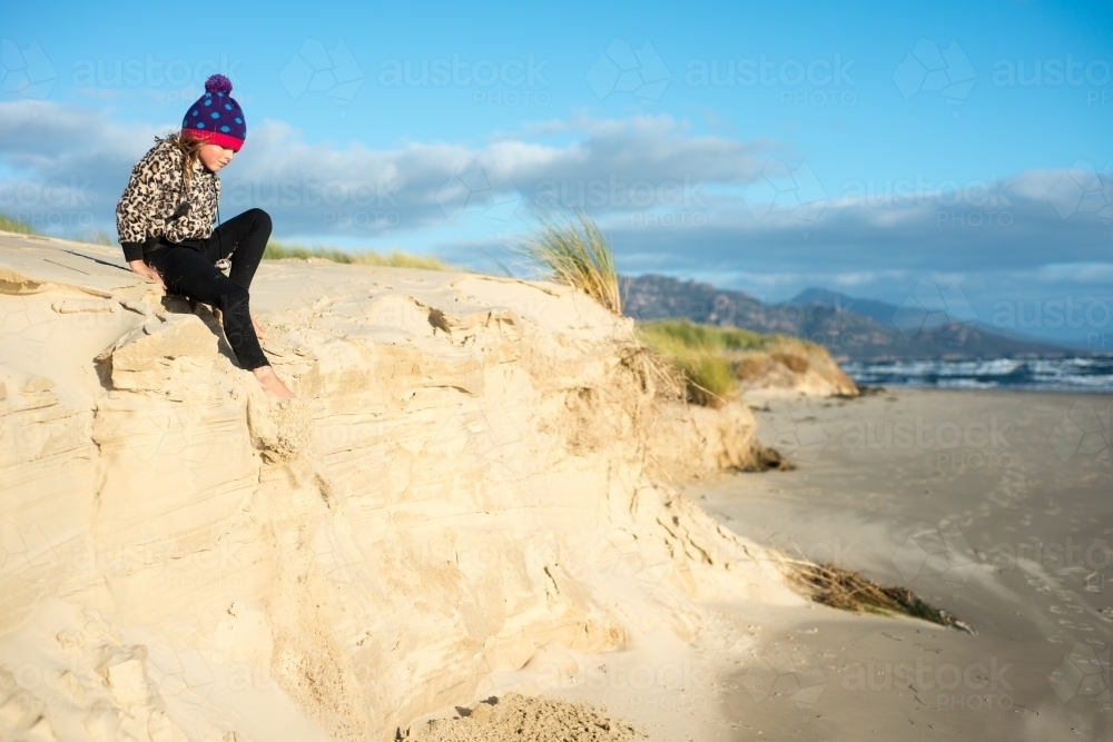 Girl climbing on sand dunes at beach late on a winter day nearly at sunset - Australian Stock Image