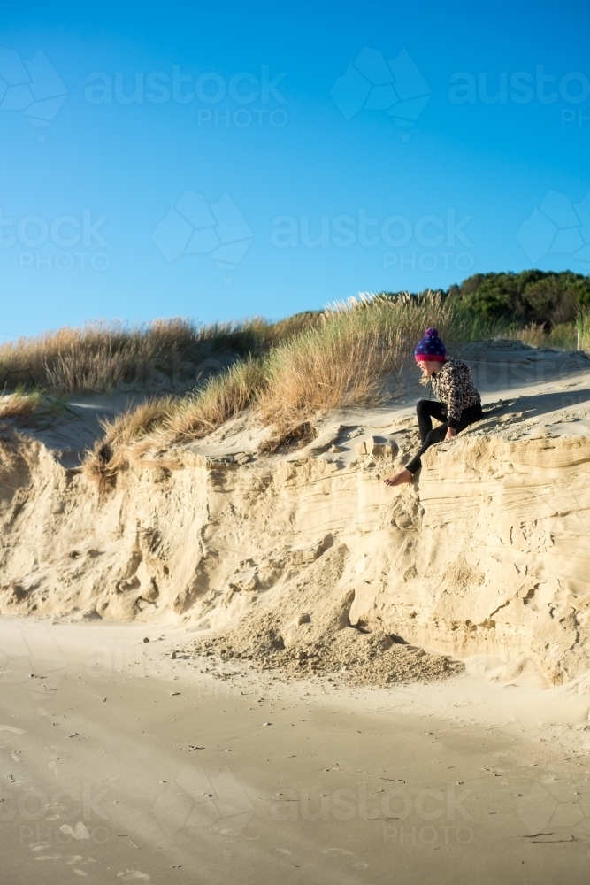 Girl climbing on sand dunes at beach late on a winter day nearly at sunset - Australian Stock Image