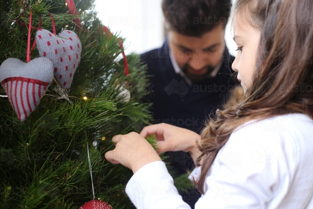 Girl decorating Christmas tree with dad in background - Australian Stock Image