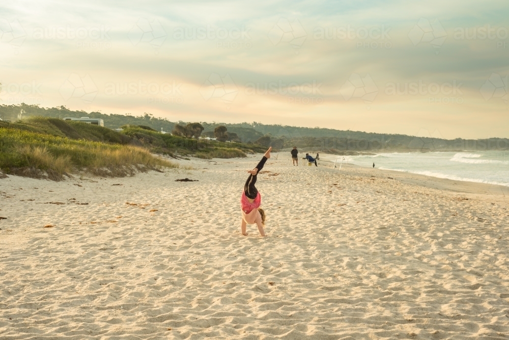 Girl doing cartwheels on a beach at sunset - Australian Stock Image