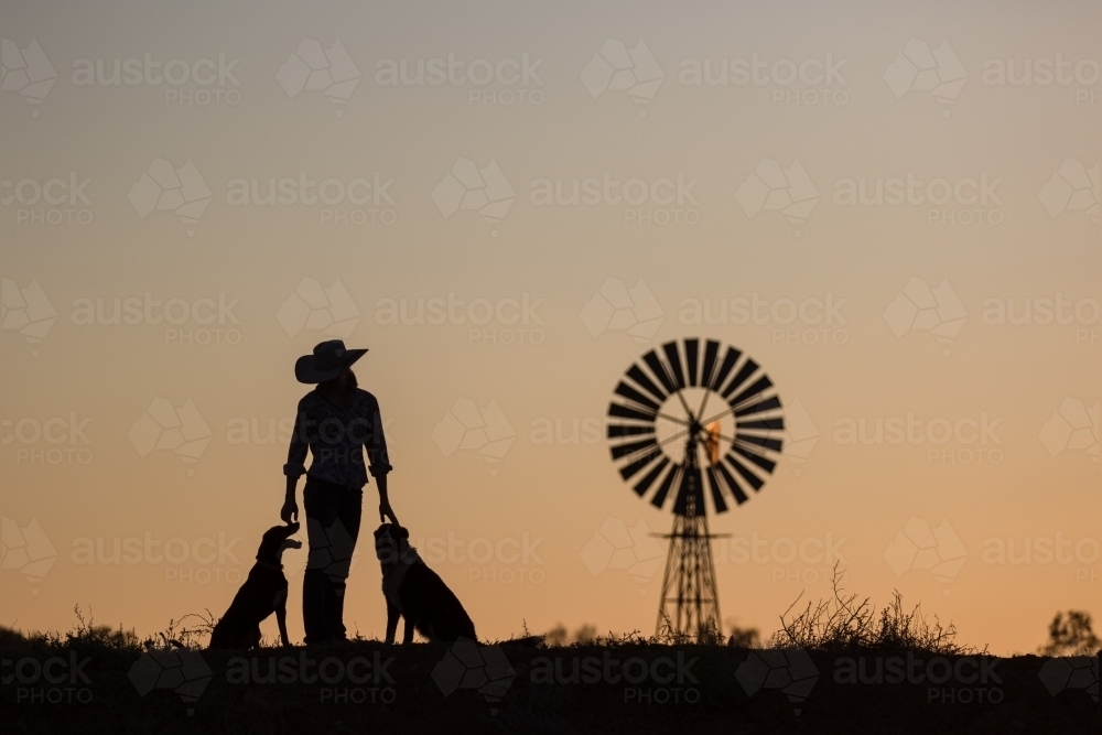 Girl farmer with dogs and windmill in silhouette - Australian Stock Image