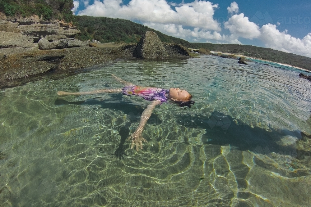 Girl floating in an ocean rockpool - Australian Stock Image