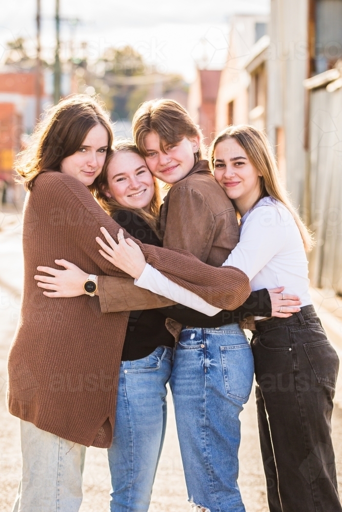 Girl friends standing cuddling and smiling - Australian Stock Image