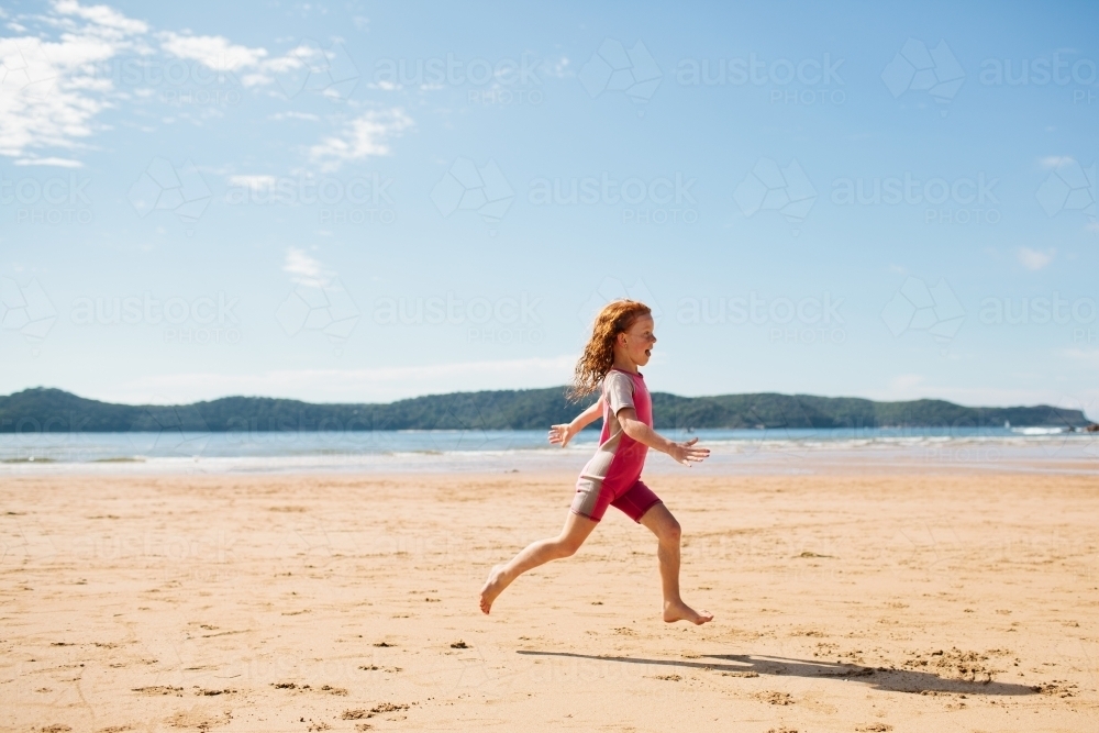 Girl in a wetsuit running on the sand at the beach - Australian Stock Image