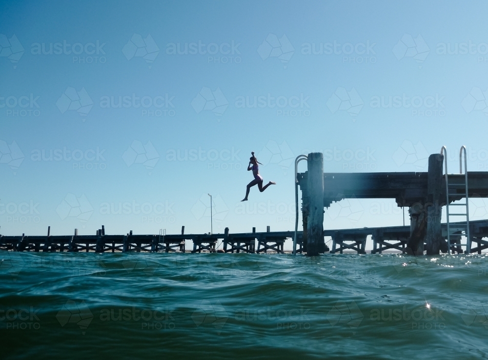 Girl jumping off jetty into ocean - Australian Stock Image