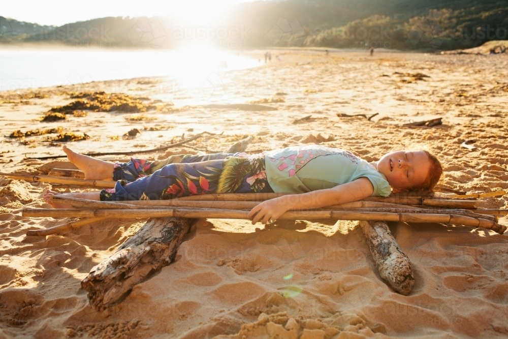 Girl laying on a bamboo raft on the beach - Australian Stock Image