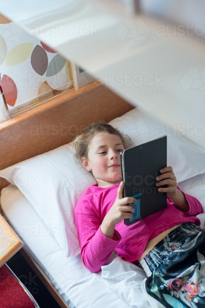 Girl laying on bunkbed looking at ipad - Australian Stock Image