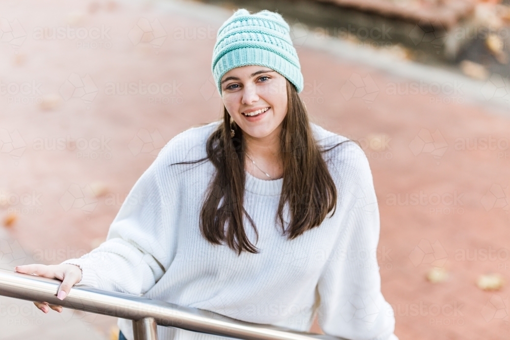 Girl leaning against hand rail smiling wearing beanie - Australian Stock Image