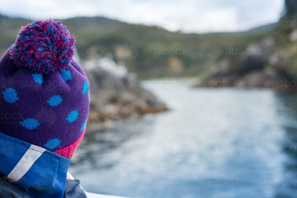 Girl looking at ocean water and rocky land from boat on a cold winter day - Australian Stock Image