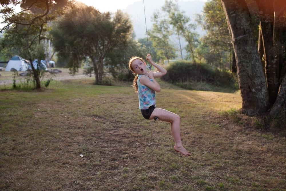 Girl playing on a rope swing at a campsite - Australian Stock Image