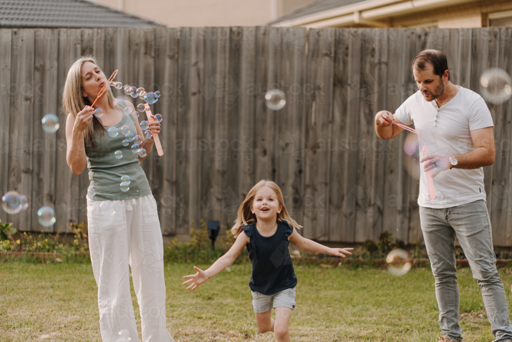 Girl playing with bubbles with mum and dad in backyard - Australian Stock Image