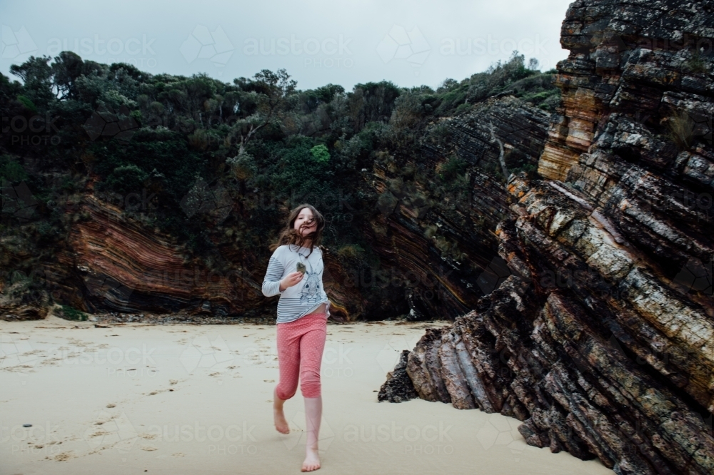 Girl running on the sand at the beach with her hair on her face - Australian Stock Image