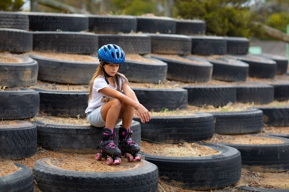 girl sitting by herself wearing roller skates and helmet - Australian Stock Image