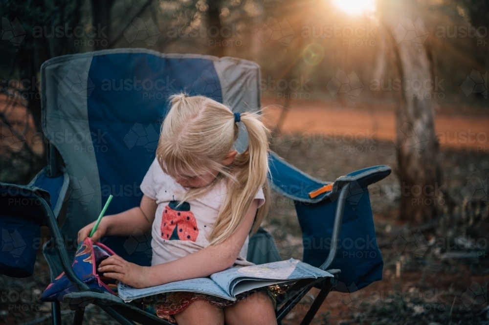 girl sitting in a camp chair at sunset drawing - Australian Stock Image