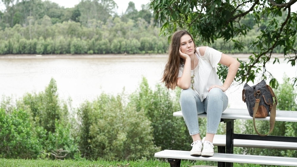 Girl sitting on park bench with bag - Australian Stock Image