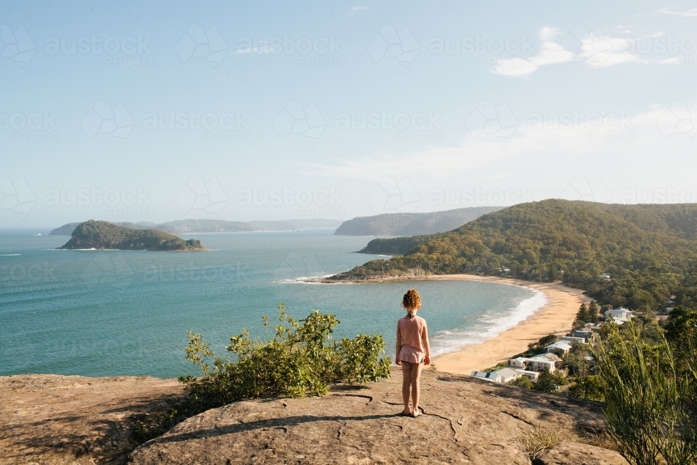 Girl standing on a rock looking at the view over a beach - Australian Stock Image