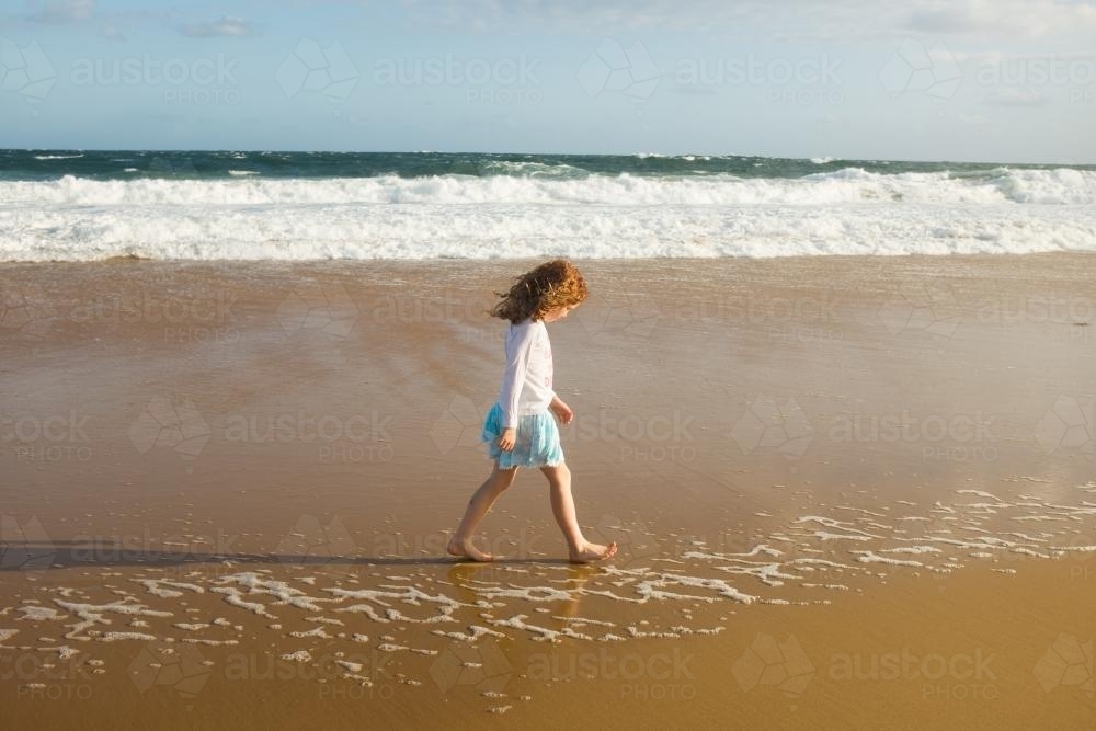 image-of-girl-walking-along-the-shoreline-at-the-beach-austockphoto