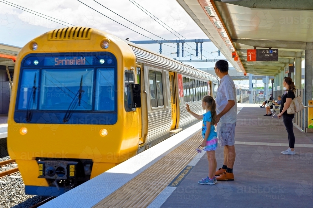 Girl waving to the train with dad standing on the platform and people waiting for train to arrive - Australian Stock Image